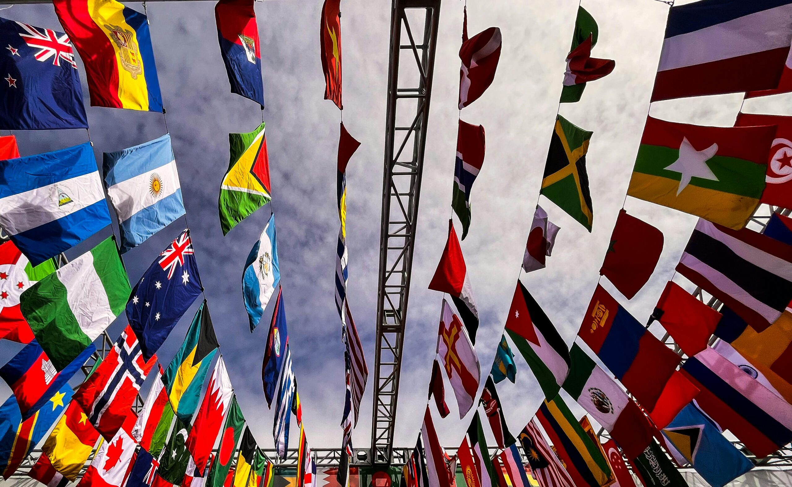A dynamic low angle shot of various international flags hanging outdoors against a cloudy sky.